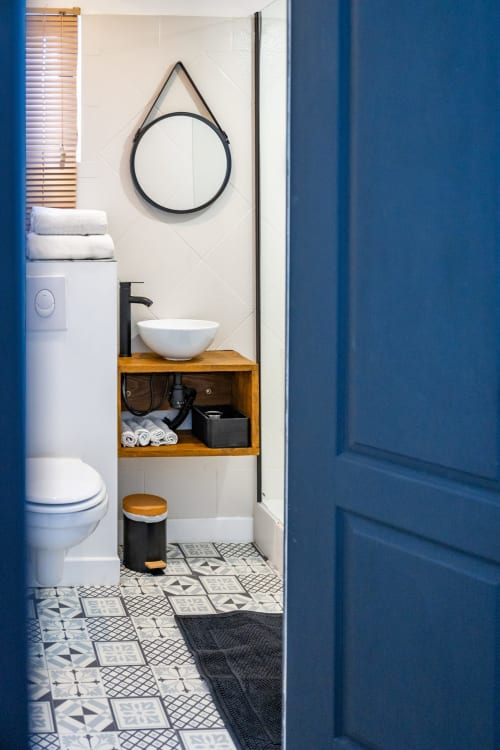 Salle de bain moderne au Domaine Mas Lafleur avec vasque, robinetterie noire, miroir rond, meuble en bois et carrelage géométrique