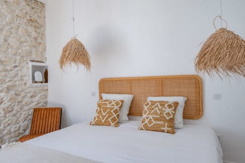 Chambre minimaliste avec tête de lit en rotin, luminaires suspendus tressés et coussins à motifs au gîte Domaine Mas Lafleur