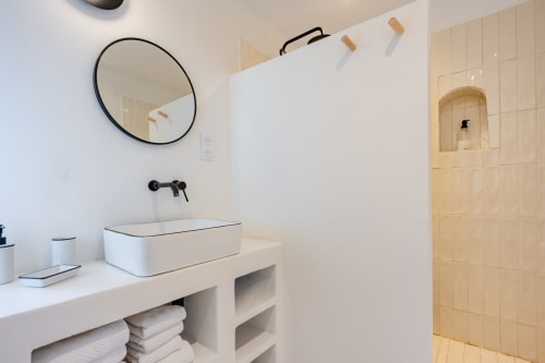Salle de bain moderne avec lavabo blanc rectangulaire, miroir circulaire et douche carrelée du gîte Domaine Mas Lafleur