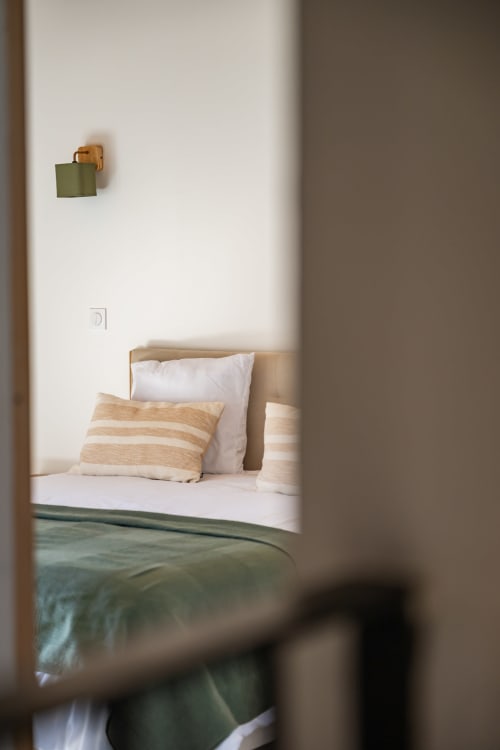 Chambre minimaliste au Domaine Mas Lafleur avec oreiller rayé, literie blanche et applique murale verte