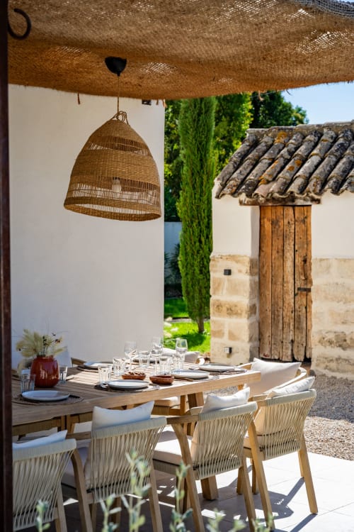 Terrasse de restauration en plein air au Domaine Mas Lafleur avec lampe suspendue tissée, table en bois et bâtiments en pierre rustique