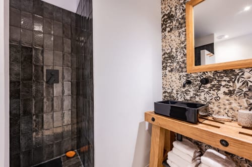 Salle de bain moderne au Domaine Mas Lafleur avec douche en carrelage noir, meuble vasque en bois et papier peint floral