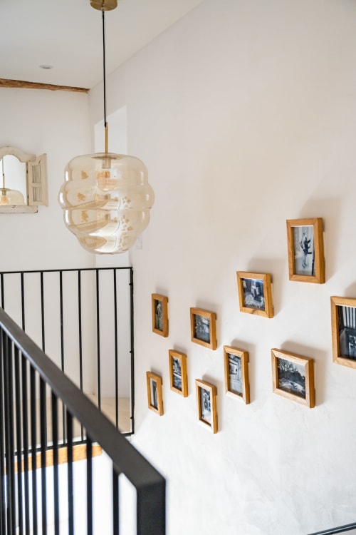 Escalier du Domaine Mas Lafleur avec suspension luminaire, rampe noire et galerie de photos encadrées