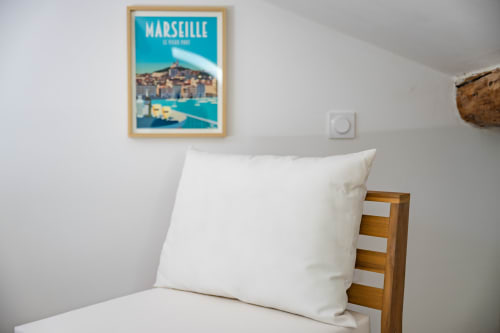 Chambre cosy du Domaine Mas Lafleur avec oreillers blancs, lit en bois et affiche de voyage Marseille au mur