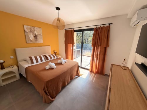 Chambre moderne de la Villa Louniceli aux Villas d'A Storia, Porto-Vecchio, avec lit en terre cuite, mur d'accent orange et patio