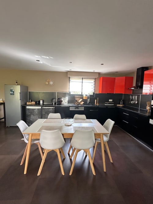 Cuisine-salle à manger contemporaine à Villa Maé : mobilier noir, accents rouges, table en bois, chaises blanches et inox