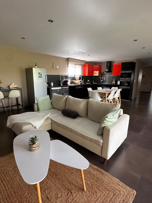 Élégant séjour ouvert de la Villa Maé avec canapé beige, table basse blanche et cuisine aux placards rouges à Ghisonaccia