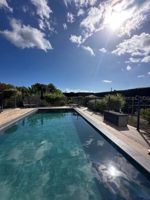 Piscine ensoleillée aux eaux turquoise aux Villas d'A Storia à Pinarellu, Corse, entourée de terrasse en bois et végétation luxuriante
