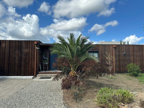 Villa Maé aux Villas d'A Storia à Ghisonaccia avec façade en bois foncé, palmier et jardin d'entrée en gravier