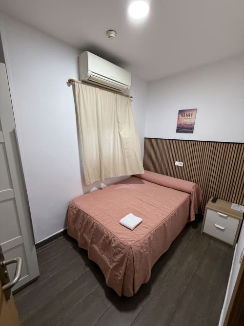 Moderna habitación doble en Hostal3hermanos en Getafe con colcha rosa, aire acondicionado y pared de madera