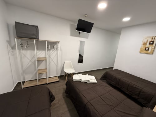 Habitación triple en Hostal3hermanos de Getafe con tres camas oscuras, TV mural, armario blanco y comodidades modernas