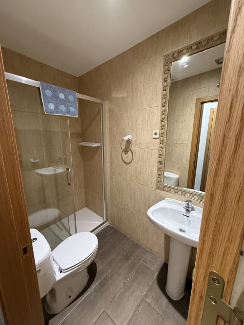 Baño moderno en Hostal3hermanos Getafe con inodoro, lavamanos pedestal, espejo y ducha con cabina independiente