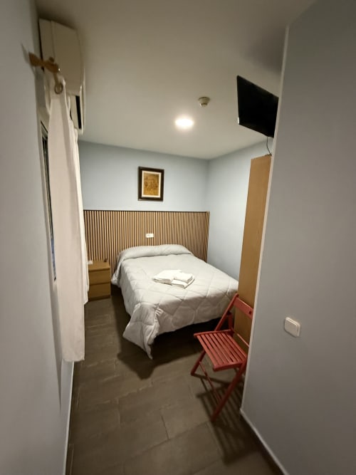 Habitación individual del Hostal 3 Hermanos en Getafe con cama, TV, silla roja y decoración minimalista moderna