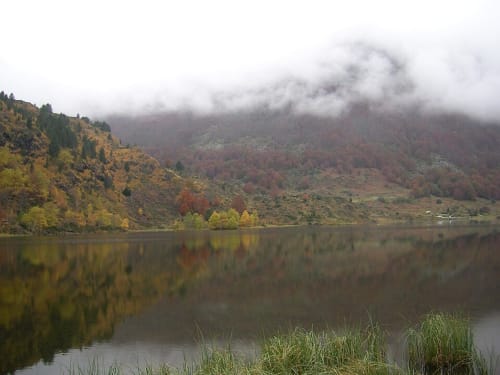 Paysage automnal brumeux à la Maison Du Haut Salat à Seix, France : un lac calme reflétant les teintes de l'automne et la forêt
