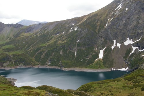 Lac de montagne alpin entouré de pentes verdoyantes et de plaques de neige près de Seix, France