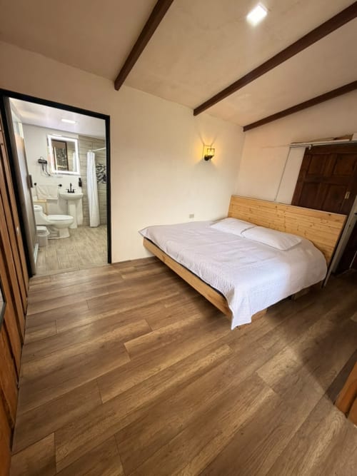Dormitorio espacioso con cama de madera, baño privado, pisos de madera dura y techo con vigas en Chalets Vistas del Poas