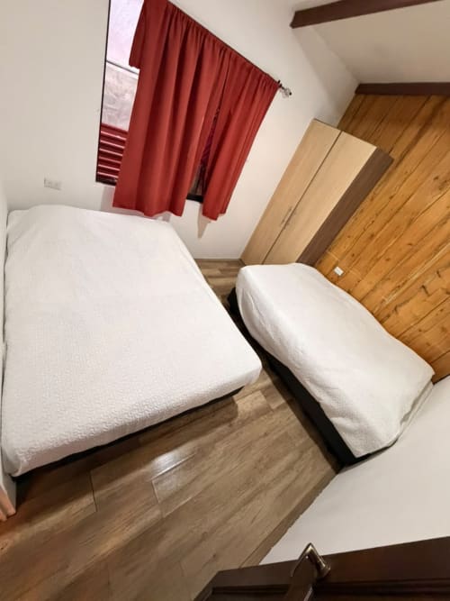 Dos camas gemelas con sábanas blancas en una habitación de villa en Chalets Vistas del Poas, Heredia, con piso de madera y cortinas rojas
