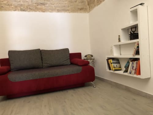 Moderno soggiorno con divano rosso e grigio, pavimento in legno, scaffali bianchi con libri e soffitto in mattoni a vista a La