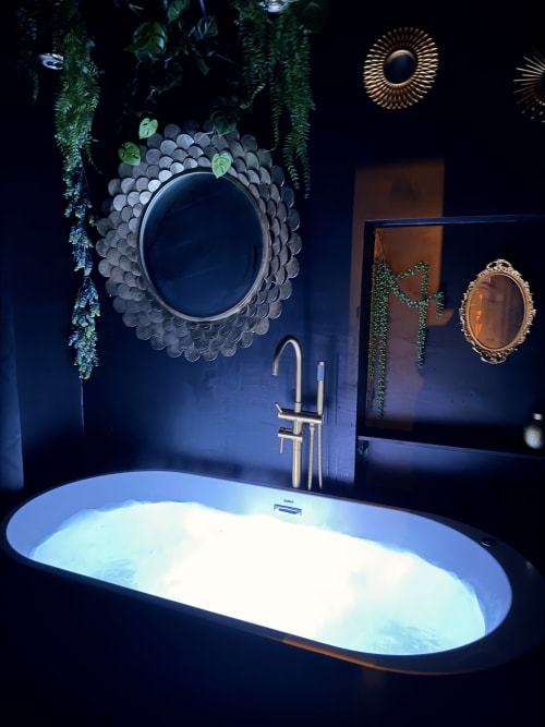 Salle de bains luxueuse à La Maison Defendue avec baignoire éclairée, miroirs décorés, plantes suspendues et finitions dorées