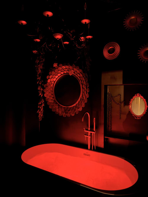 Salle de bain luxueuse aux lumières rouges à La Maison Defendue avec miroirs décoratifs, suspensions et baignoire ilôt moderne