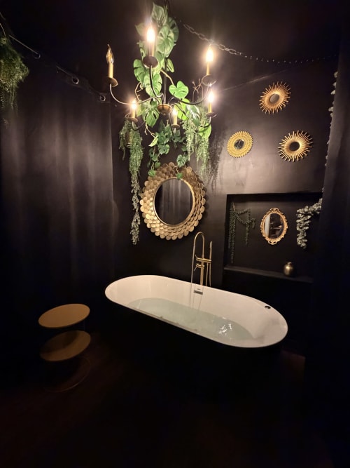 Salle de bain luxueuse du gîte La Maison Defendue avec baignoire îlot blanche, miroirs dorés et décoration botanique
