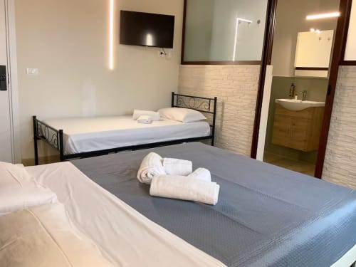 Chambre triple moderne au Sikania Agri Relais à Caccamo avec deux lits, serviettes roulées, télévision et salle de bain attenante avec vue montagne
