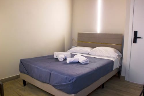 Lit double moderne de la chambre Sikania Agri Relais avec tête de lit grise, oreillers blancs, serviettes roulées et vue montagne