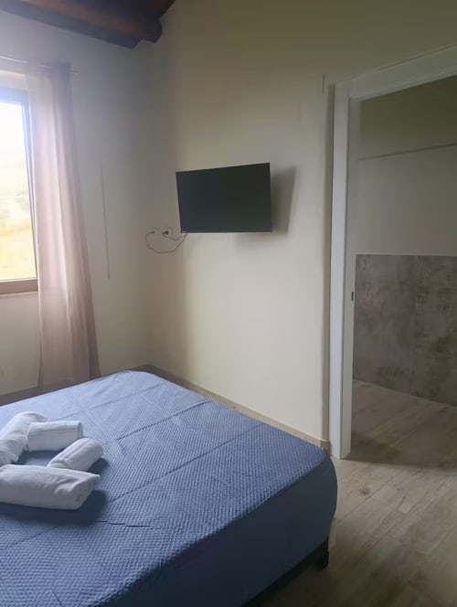 Chambre lumineuse au Sikania Agri Relais de Caccamo avec lit bleu, TV murale et vue sur les montagnes