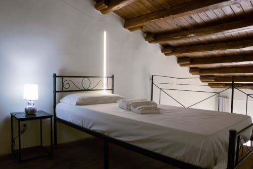 Chambre rustique au Sikania Agri Relais avec lit en métal noir, poutres apparentes, vue sur la montagne et lampe de chevet