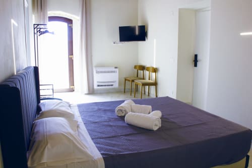 Chambre d'hôtel lumineuse au Sikania Agri Relais avec lit, télévision, chaises en bois et vue sur les montagnes