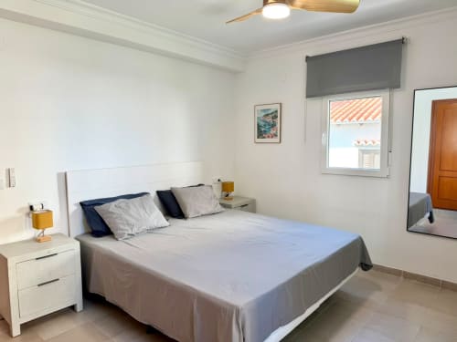 Dormitorio luminoso en la casa rural Casa Mar Blau, Valencia, con vistas al mar, cama blanca, ventilador de techo de madera y acceso a balcón
