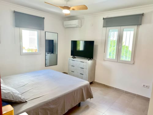 Dormitorio luminoso en la Casa Mar Blau en Valencia con cama doble, televisor, cómoda y vistas al mar desde las ventanas