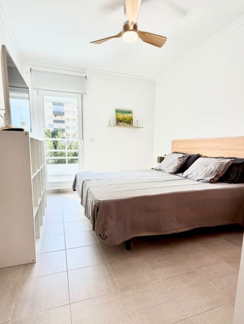 Dormitorio moderno en Casa Mar Blau, Valencia, con cama de madera, ventilador de techo y acceso a balcón con vistas al mar