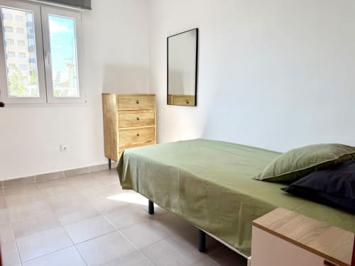 Dormitorio luminoso con ropa de cama verde, cómoda de madera, espejo y vistas al mar en la casa rural Casa Mar Blau en Valencia