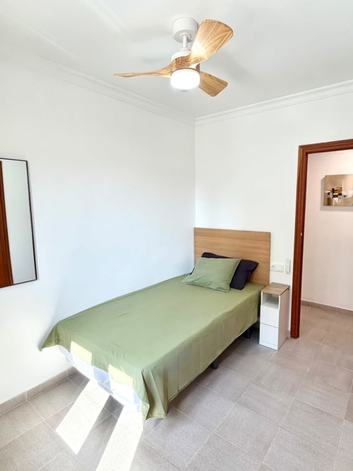 Luminoso dormitorio con cama individual, cabecero de madera y ventilador de techo en la cabaña Casa Mar Blau de Valencia