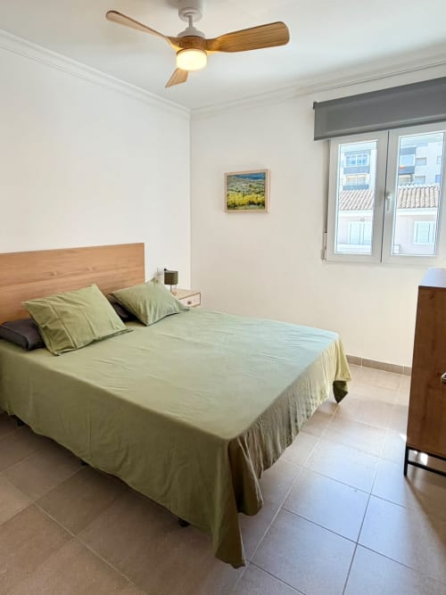 Dormitorio luminoso en casa rural Casa Mar Blau, Valencia, con cama de madera, ropa de cama verde, ventilador de techo y vistas al mar