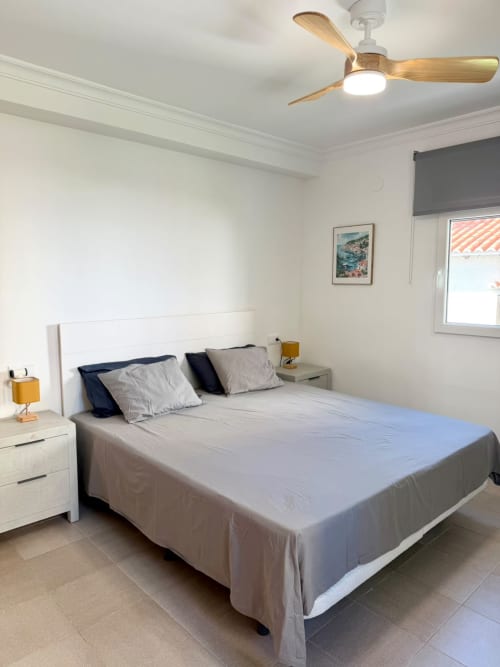 Dormitorio moderno con cama blanca, ventilador de techo de madera y vistas al mar en la casa de vacaciones Casa Mar Blau en Valencia