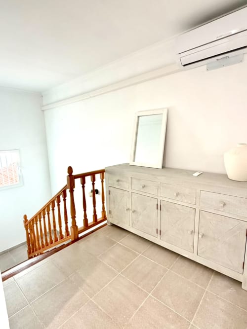 Luminosa habitación costera con cuna de madera, cómoda de madera clara, espejo y piso de baldosas beige en Stay Gest Valencia