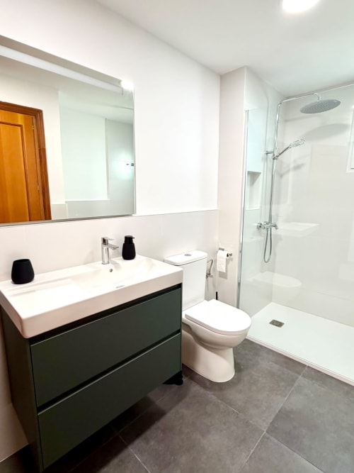 Baño moderno en la casa rural Casa Mar Blau, Valencia con suelo de baldosas oscuras, lavabo blanco, inodoro y ducha con mampara de cristal