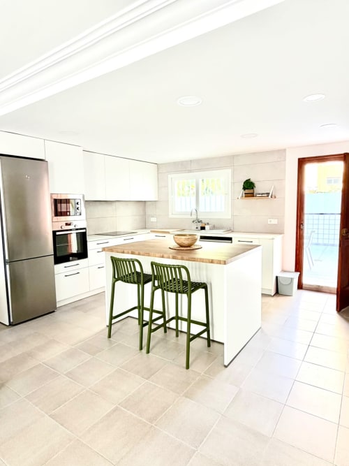 Cocina moderna blanca con isla, taburetes verdes y encimera de madera en la casa de campo Casa Mar Blau de Valencia