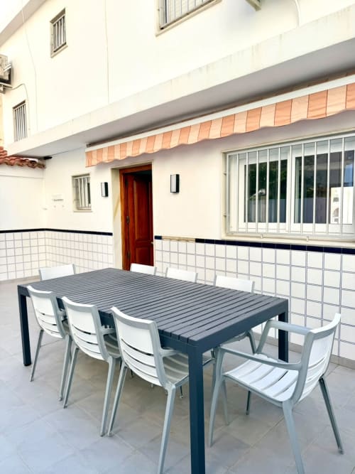 Área de comedor al aire libre en la casa de campo Casa Mar Blau en Valencia, con mesa moderna y sillas blancas junto a puerta roja