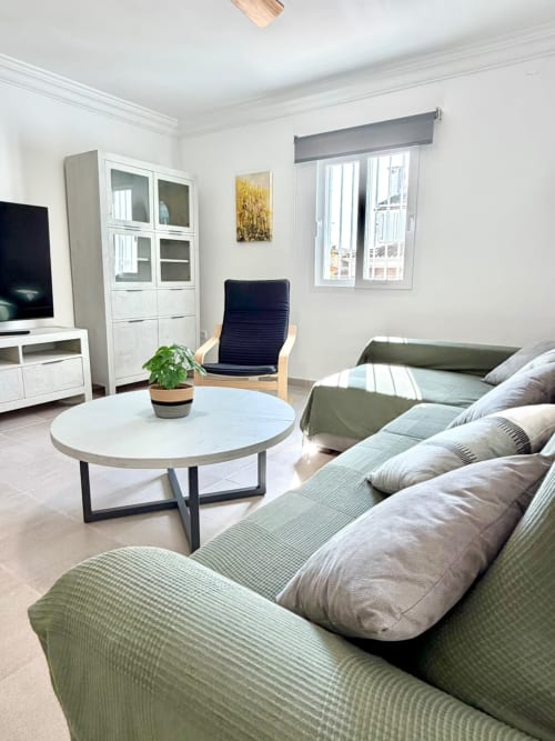 Sala de estar moderna de la casa rural Casa Mar Blau en Valencia con vistas al mar, sofá verde, mesa redonda blanca y luz natural