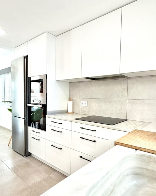 Cocina moderna blanca con electrodomésticos de acero inoxidable, encimera negra, backsplash beige y mesa de madera en Casa Mar