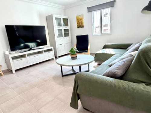Sala de estar moderna en la casa rural Casa Mar Blau, Valencia, con sofá verde salvia, mueble TV blanco y mesa de centro redonda