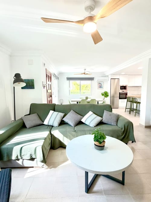 Sala moderna de la casa rural Casa Mar Blau en Valencia con sofá verde en L, mesa redonda blanca y vistas al mar desde