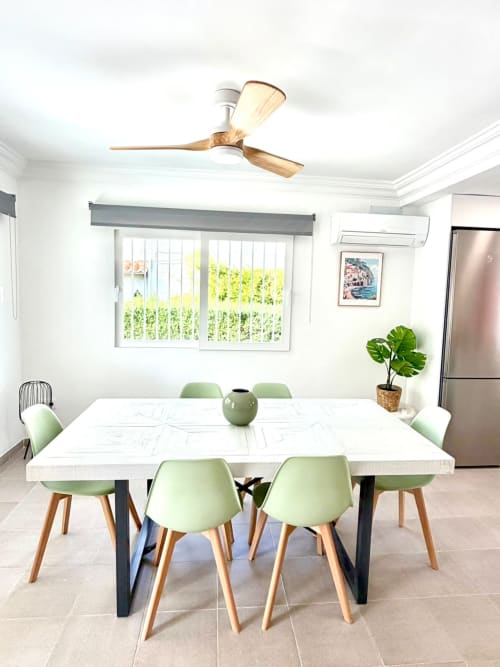 Comedor moderno con mesa blanca, sillas verdes, ventilador de techo y vistas al mar en la casa de vacaciones Casa Mar Blau en Valencia