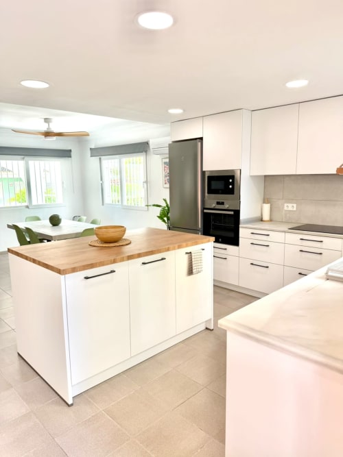 Cocina moderna blanca con isla de madera, electrodomésticos de acero inoxidable y zona de comedor en Casa Mar Blau, Valencia