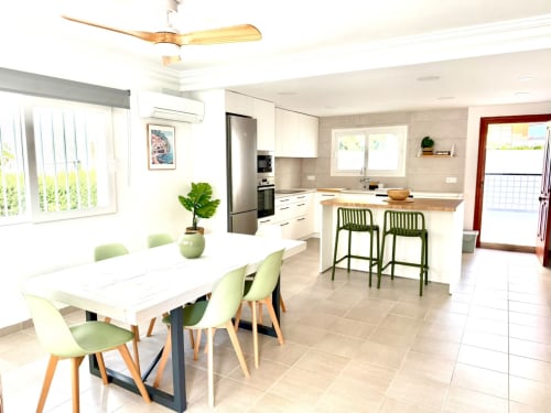 Cocina y comedor modernos en la casa rural Casa Mar Blau, Valencia, con muebles blancos, mesa de comedor, barra y vistas al mar