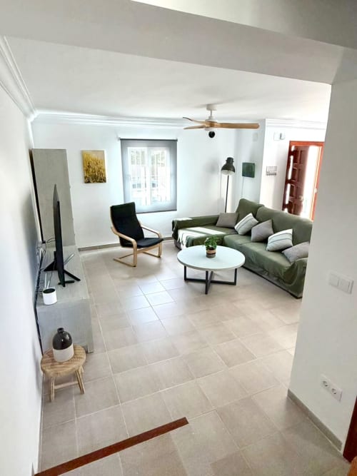 Sala moderna de la casa rural Casa Mar Blau en Valencia con sofá oliva, mesa redonda blanca y acceso a vistas al mar