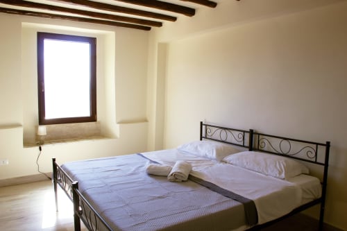Chambre lumineuse du Sikania Agri Relais à Caccamo avec vue montagne, lit en métal noir, draps blancs, poutres en bois